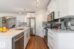 Spacious kitchen featuring white cabinetry, stainless steel appliances, a large center island with an undermount sink, a mosaic tile backsplash, and wood-finish flooring - 