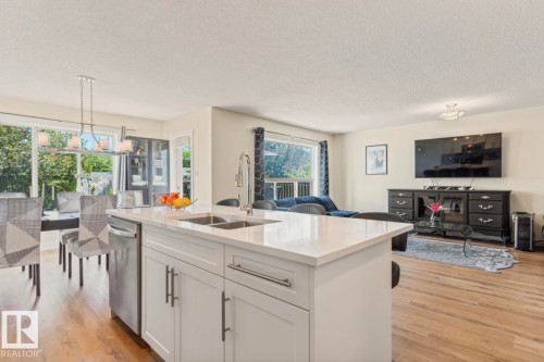 Kitchen island featuring a double-basin sink, stainless steel faucet, and white cabinetry with brushed nickel hardware - 1007 Macewan Cl, Edmonton, AB 