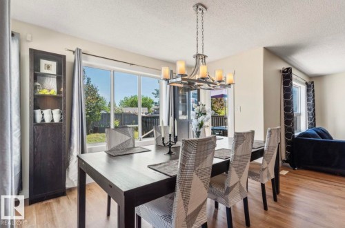 Dining area featuring wood-finish flooring, a contemporary chandelier, and a built-in shelving unit - 1007 Macewan Cl, Edmonton, AB 