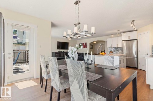 Dining area featuring wood-finish flooring, a modern chandelier, and a glass-paneled door leading to a wood-plank deck - 1007 Macewan Cl, Edmonton, AB 