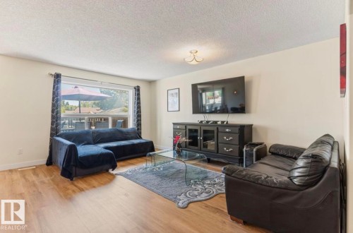Spacious living area featuring wood-finish flooring, a large picture window, and a ceiling-mounted light fixture - 1007 Macewan Cl, Edmonton, AB 