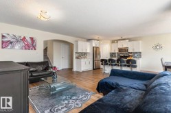 Open-concept living area featuring wood-finish flooring throughout, a kitchen with white cabinetry, stainless steel appliances, and a tiled backsplash, and an arched doorway - 