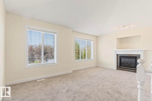 Carpeted room featuring two windows with blinds, a fireplace with a white mantel and stone surround, and track lighting - 1007 Macewan Cl, Edmonton, AB 
