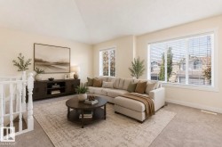 Spacious living area featuring light-toned walls, neutral carpeting, and multiple windows - 