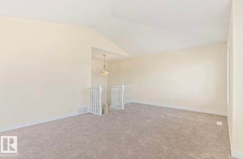 Spacious open area featuring sloped ceilings, plush gray carpeting, white trim, and a decorative pendant light fixture highlighting the banister - 1007 Macewan Cl, Edmonton, AB 