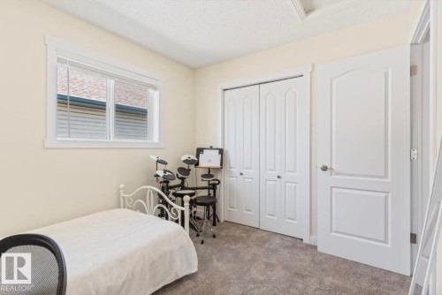 Neutral-toned room featuring a single window with blinds, bi-fold closet doors, a white paneled door, and textured carpet flooring - 1007 Macewan Cl, Edmonton, AB 
