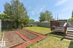 Expansive backyard featuring a raised wood deck with baluster railing, a dedicated garden bed area, mature trees, and privacy fencing - 