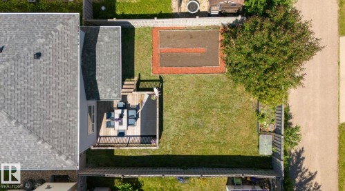 Expansive backyard featuring a natural wood-finish deck with railings, a manicured lawn, a cultivated garden bed, and a mature tree - 1007 Macewan Cl, Edmonton, AB 