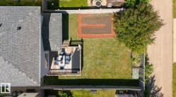 Expansive backyard featuring a natural wood-finish deck with railings, a manicured lawn, a cultivated garden bed, and a mature tree - 