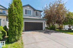 Two-story residence featuring light gray siding, a dark gray garage door, and a concrete driveway - 