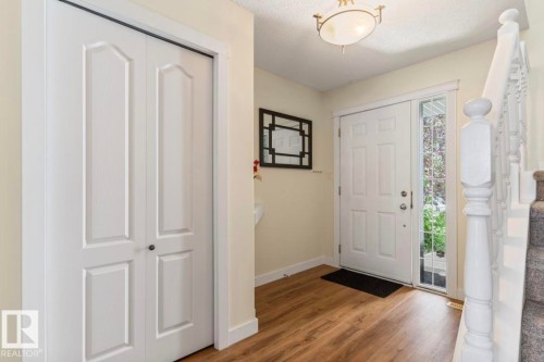 Entryway featuring wood-finish flooring, a white paneled front door with a sidelight, a white bi-fold closet, and a carpeted staircase with white balusters - 1007 Macewan Cl, Edmonton, AB 