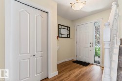Entryway featuring wood-finish flooring, a white paneled front door with a sidelight, a white bi-fold closet, and a carpeted staircase with white balusters - 