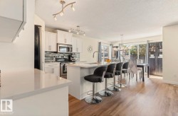Open-concept kitchen and dining area featuring white cabinetry, light-toned countertops, stainless steel appliances, a multi-toned backsplash, and wood-finish flooring - 