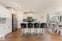 Open-concept kitchen featuring white cabinetry, stainless steel appliances, a multi-tone tile backsplash, and a central island with countertop seating - 