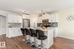 Modern kitchen featuring white cabinetry, stainless steel appliances, a mosaic tile backsplash, a central island with a sink, and wood-finish flooring - 
