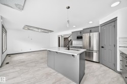 Open-concept kitchen and living area featuring a central island with a light-toned countertop, gray cabinetry, stainless steel appliances, and wood-finish flooring - 