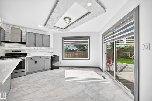 Modern kitchen featuring stainless steel appliances, grey shaker cabinetry, white subway tile backsplash, and light-toned stone-finish flooring - 1549 37C Avenue, Edmonton, AB 