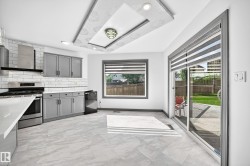 Modern kitchen featuring stainless steel appliances, grey shaker cabinetry, white subway tile backsplash, and light-toned stone-finish flooring - 