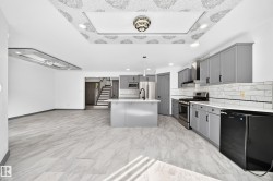 Open concept kitchen and living area featuring grey cabinetry, white countertops, stainless steel appliances, and a central island with a sink - 