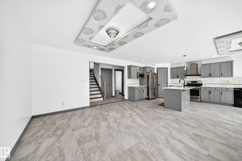 Open-concept living space featuring a contemporary kitchen with gray cabinetry, white subway tile backsplash, and stainless steel appliances - 1549 37C Avenue, Edmonton, AB 