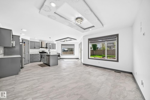 Open-concept living area featuring a modern kitchen with gray cabinetry, a central island with a sink, stainless steel appliances, and a subway tile backsplash - 1549 37C Avenue, Edmonton, AB 