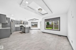 Open-concept living area featuring a modern kitchen with gray cabinetry, a central island with a sink, stainless steel appliances, and a subway tile backsplash - 