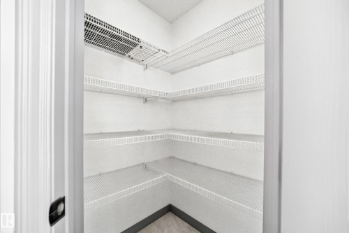 Corner pantry featuring multiple levels of wire shelving, white wall finishes, and a dark baseboard trim - 1549 37C Avenue, Edmonton, AB 