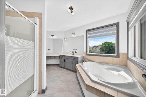 Spacious bathroom featuring a corner soaking tub with tile surround, a separate glass-enclosed shower, dual vanity with shaker-style cabinetry and stone-finish countertops, and large windows - 1549 37C Avenue, Edmonton, AB 