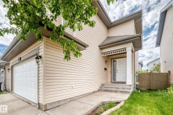 Cream-toned siding exterior featuring a covered entry, concrete steps, and an attached single-car garage with a paneled door - 
