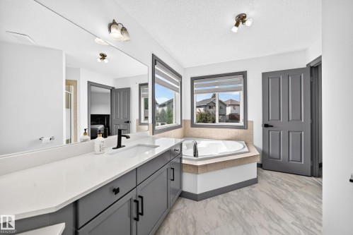 Bathroom featuring a long dual vanity with a white countertop and gray cabinetry, a built-in corner bathtub, and two windows - 1549 37C Avenue, Edmonton, AB 