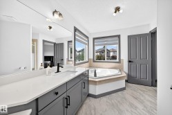 Bathroom featuring a long dual vanity with a white countertop and gray cabinetry, a built-in corner bathtub, and two windows - 