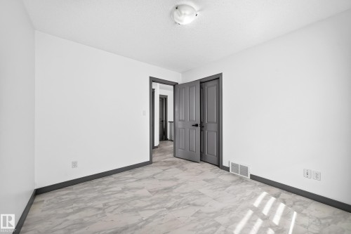 Tile flooring with a marble-effect pattern, contrasting dark baseboards, and a neutral white wall color - 1549 37C Avenue, Edmonton, AB 