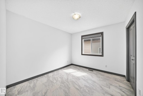 Room featuring light-toned walls, wood-finish flooring with a marble-like pattern, and dark contrasting baseboards - 1549 37C Avenue, Edmonton, AB 