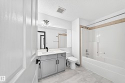 Bathroom featuring a white tub and shower combination with tan tile surround, a gray vanity with an integrated sink and black faucet, a large wall-mounted mirror, and marble-look floor tiles - 