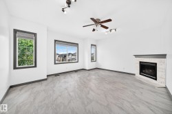 Spacious living area featuring light-toned tile flooring, a built-in fireplace with a stone-look surround, and a ceiling fan - 