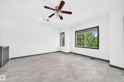 Spacious room featuring light-toned tile flooring, contemporary baseboards, and a dark wood-finish ceiling fan - 