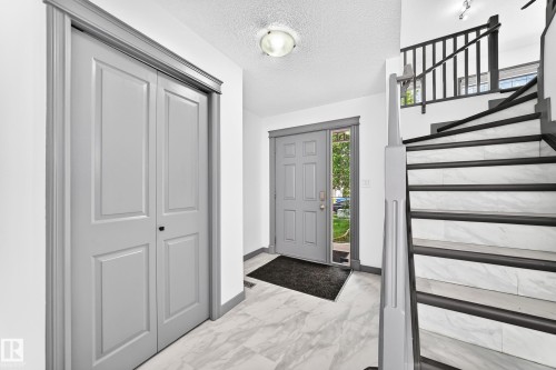 Foyer featuring gray panel doors, marbled tile flooring, and a staircase with white risers and dark treads - 1549 37C Avenue, Edmonton, AB 