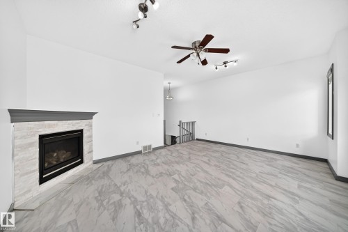 Spacious room featuring light-toned wood-finish flooring, a contemporary fireplace with a stone-look surround and dark mantel, a ceiling fan, track lighting, and white painted walls - 1549 37C Avenue, Edmonton, AB 