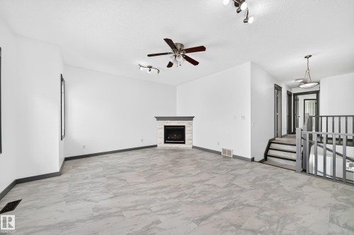 Spacious room featuring light-toned tile flooring, a fireplace with a light-toned stone surround, and a dark wood mantel - 1549 37C Avenue, Edmonton, AB 