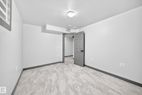 Spacious room featuring light gray walls, dark gray baseboards, and wood-finish flooring - 1549 37C Avenue, Edmonton, AB 