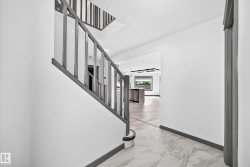 Hallway entrance featuring marble-look tile flooring and a gray-painted staircase with vertical balusters - 1549 37C Avenue, Edmonton, AB 