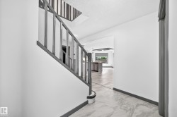 Hallway entrance featuring marble-look tile flooring and a gray-painted staircase with vertical balusters - 