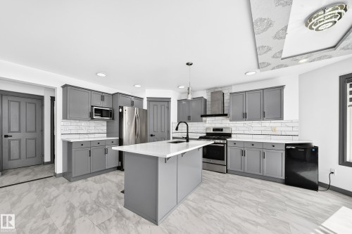 Open-concept kitchen featuring an island with a white countertop, gray cabinetry, stainless steel appliances, and a patterned ceiling detail - 1549 37C Avenue, Edmonton, AB 