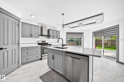 Modern kitchen featuring light gray cabinetry, stainless steel appliances, a center island with sink, white subway tile backsplash, and light-toned flooring - 1549 37C Avenue, Edmonton, AB 
