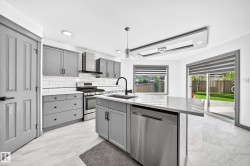 Modern kitchen featuring light gray cabinetry, stainless steel appliances, a center island with sink, white subway tile backsplash, and light-toned flooring - 