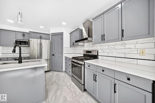 Kitchen featuring gray cabinetry with black hardware, white countertops, stainless steel appliances, and wood-finish flooring - 1549 37C Avenue, Edmonton, AB 
