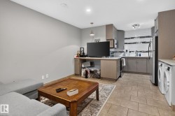 Open-concept living space featuring a modern kitchen with grey cabinetry, subway tile backsplash with accent strips, and a stainless steel sink - 
