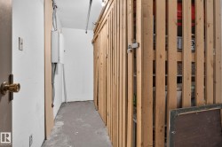 Storage area with concrete flooring, white painted walls, exposed electrical conduit, and a slatted wood storage enclosure - 