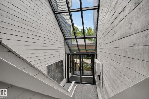 Slanted glass roofline over an entry area with double glass doors, flanked by white horizontal siding walls - G14 10148 118 Street Nw, Edmonton, AB 