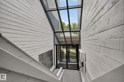 Slanted glass roofline over an entry area with double glass doors, flanked by white horizontal siding walls - 